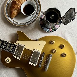 Zlatá elektrická kytara s tvarem singlecut, krémovým pickguardem a dvěma humbuckery. Na kytaru jsou vidět drobné škrábance a opotřebení povrchu. Vedl…