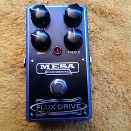 Modrý efekt pedál s černým horním panelem. Na panelu jsou nápisy FLUX-DRIVE, MESA ENGINEERING a popisky ovladačů BASS a TREBLE. Zařízení má čtyři čer…