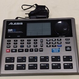 Stříbrný bicí automat značky Alesis, model SR18. Na předním panelu je nápis HIGH DEFINITION STEREO MULTI-SAMPLED DRUM MACHINE WITH DYNAMIC ARTICULATI…