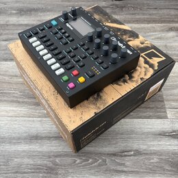 Černý digitální sekvencer a syntetizátor s nápisem Digitone, umístěný na originální krabici s nápisy Digitone a FM digital drum machine. Zařízení má…