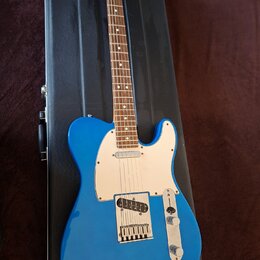 Modrá elektrická kytara typu Telecaster s bílým pickguardem a hnedým hmatníkem, položená na černém tvrdém kufru. Nástroj má dva snímače a dva ovládac…
