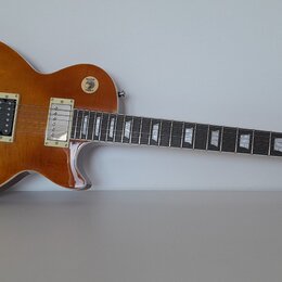 Elektrická kytara typu Les Paul v jantarové barvě s viditnou strukturou dřeva. Na hmatníku jsou trapezoidové vložky a na hlavě je nápis Gibson. Kytar…