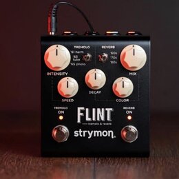 Černý efekt pedál s bílými ovládacími knoflíky. Na předním panelu jsou nápisy TREMOLO, REVERB, INTENSITY, MIX, SPEED, DECAY a COLOR. Uprostřed je vel…