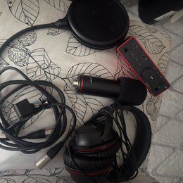 Sada audio vybavení položená na vzorovaném podkladu. Obsahuje červený zvukový interface s nápisem Scarlett 2i2, černý mikrofon s nápisem Scarlett, če…