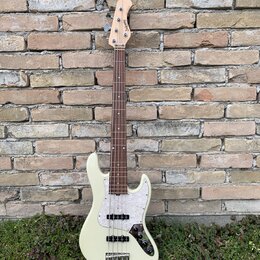 Bílá elektrická basová kytara s tmavým hmatníkem a bílým pickguardem. Na hlavě nástroje je viditelné logo "Squier". Kytara má čtyři struny a stříbrný…