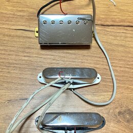 Tři elektrické snímače kytary s kovovými kryty v stříbrné barvě, umístěné na dřevěném povrchu. Horní snímač je typu humbucker s šesti viditelnými pol…