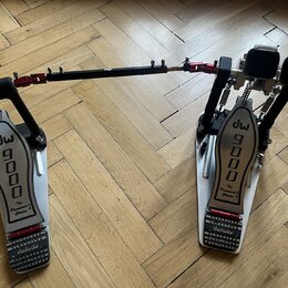 Dvojpedál na bicí v bílo-černo-červené barevné kombinaci s kovovými plátmi. Na obou plátích je černý nápis dw 9000 a pod ním text The Drummer's Choic…