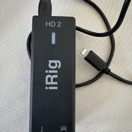 Černý obdélníkový adaptér s nápisy HD 2 a iRig. Zařízení má připojený USB kabel a jeden volný konektor Lightning. V dolní části jsou vyznačené ikony…