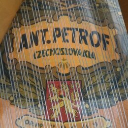Detailní pohled na dřevěný nástroj s napnutými strunami. Na povrchu je vidět dekorativní nápis ANT. PETROF a pod ním text CZECHOSLOVAKIA. Ve spodní č…