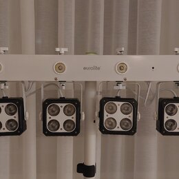 Bílá světelná lišta s čtyřmi černými LED moduly, z nichž každý obsahuje čtyři čočky. Na horní bílé části je umístěn nápis eurolite. Zařízení je upevn…