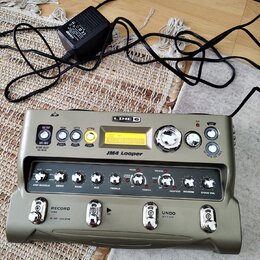 Šedo-zelený looper s nápisy LINE 6 a JM4 Looper. Zařízení obsahuje řadu ovládacích knoflíků, tlačítek a malý displej s textem STYLE: EASY. Ve spodní…