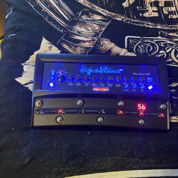 Černý kytarový procesor s modrým podsvícením tlačítek a nápisů. Na horní části je modré logo Hughes & Kettner a modelový název Black Spirit 200. Zaří…