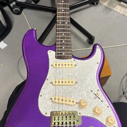 Elektrická kytara s trupem v purpurové barvě s metalickým efektem a bílým perleťovým pickguardem. Nástroj má tři zlaté snímače, tři zlaté ovládací kn…