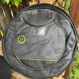 Černý kulatý polstrovaný obal na hudební nástroj s rukojetí. Na přední straně je kulatý štítek s nápisem ROCKBAG a textem "ROCKBAG by THE MUSIC GROUP…