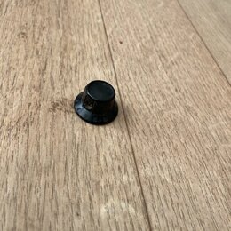 Černý plastový knoflík s kulatým základním tvarováním. Na spodní části je viditelný nápis G. l. 01 a písmeno R. Povrch vykazuje mírné známky opotřebe…