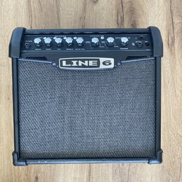 Černý kytarový kombo zesilovač značky LINE 6. Horní ovládací panel obsahuje několik otočných potenciometrů s popisky DRIVE, BASS, MID, TREBLE, CHAN V…