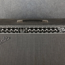 Kytarový kombozesilovač v černém potahu s textilní maskou. Na ovládacím panelu jsou nápisy NORMAL, VIBRATO a Twin Reverb-Amp, dále značka FENDER MUSI…
