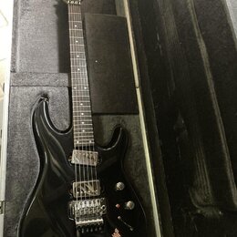 Černá elektrická kytara v tvrdém kufru. Na hlavě hmatníku je bílý nápis HAMER. Kytara má dva humbuckery, jeden ovládací knoflík hlasitosti a jeden tó…