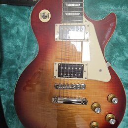 Elektrická kytara typu Les Paul s červeně-žlutým sunburst lakem a viditnou strukturou dřeva. Na hmatníku jsou vidět vložky ve tvaru trapézů a na těle…