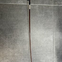 Fotografie znázorňuje smyčec s hnědým dřevěným tětivem a bílými vlasy. Horní část obsahuje černý kousek s kovovými prvky a šroubem pro napnutí. Povrc…
