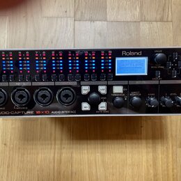 Černá racková audio rozhraní s nápisem Roland a STUDIO-CAPTURE 16x10 AUDIO INTERFACE. Zařízení má v horní části řadu barevných LED indikátorů hladiny…
