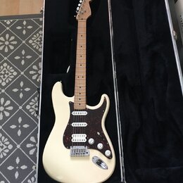 Elektrická kytara s krémovým trupem a hnědým javorovým hmatníkem v černém tvrdém kufru. Nástroj má tmavě červený pickguard, tři snímače a bílé ovláda…