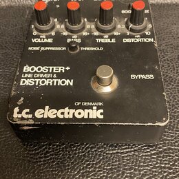 Černý efekt pedál s nápisy BOOSTER+ LINE DRIVER & DISTORTION a logem t.c. electronic OF DENMARK. Horní panel obsahuje čtyři červené oválné knoflíky s…