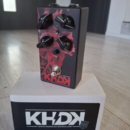 Černý kytarový efekt s červeným grafickým motivem a čtyřmi černými otočnými ovladači. Na horní straně jsou nápisy GAIN, VOLUME, BASS a TREBLE, v doln…