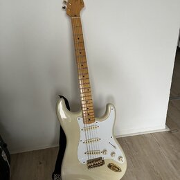Elektrická kytara s bílým trupem, bílým pickguardem a světle hnědým hnedobělým hmatníkem. Na hlavě je nápis "Fender" a v dolní části hmatníku u 12. p…