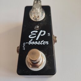 Černý kytarový efekt pedál s bílým nápisem „EP-booster“ a malým nápisem „IN“ u horního vstupu a „OUT“ u spodního výstupu. Na horní straně je umístěn…