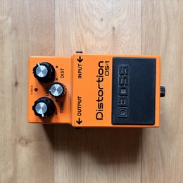 Oranžový efekt pedál s černým spínacím tlačítkem. Na zařízení jsou nápisy Distortion DS-1 a BOSS, dále popisky ovládacích prvků DIST, LEVEL a TONE a…