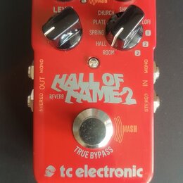 Červený efekt pedál s nápisy tc electronic, HALL OF FAME 2 a REVERB. Obsahuje čtyři černé oválné ovládací knoflíky, jeden stříbrný kovový spínač a ma…