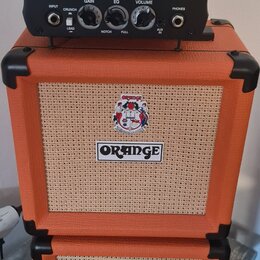 Černý kytarový zesilovač s nápisy Peavey a 6505 PIRANHA™ stojí na dvou oranžových reproduktorových boxech značky ORANGE. Zesilovač má ovládací prvky…
