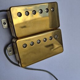Dva humbuckery s gold povrchem a viditelnými šrouby v polosách. Povrch vykazuje drobné škrábance a známky opotřebení. Z obou snímačů vedou šedé vodič…