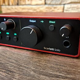 Červený audio rozhraní s černým předním panelem. Na panelu jsou nápisy Output, Direct a Scarlett Solo, čtyři otočné ovladače a několik malých zelenýc…