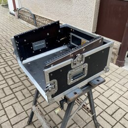 Černý transportní flightcase s hliníkovými hranami a vrchním víkem otevřeným do strany. Uvnitř jsou vidět montážní lišty pro rackové zařízení a kovov…