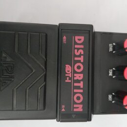 Černý kytarový efekt pedál s nápisy DISTORTION a ADT-1 v červené barvě. Na levé části je vyražen nápis ARIA a dekorativní vlnité linky. Pravá část ob…