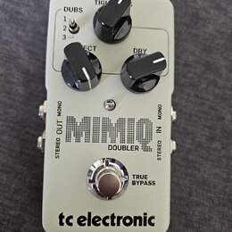 Šedý kytarový efekt s nápisem MIMIC DOUBLER a logem tc electronic. Na horní části jsou tři černé otočné ovladače s popisky TIGHT, ECT a DRY a přepína…
