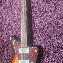 Elektrická kytara s trupem v přechodovém žlutě-červeném odstínu a hnědým hmatníkem. Na hlavě je nápis Squier by Fender. Kytara má červený vzorovaný p…