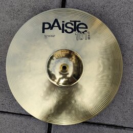 Zlatý mosazný činel typu hi-hat s koncentrickým žebrováním povrchu. Na povrchu je černý nápis pAiste, označení 101 BRASS a text 14" HI-HAT TOP. Povrc…