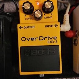 Žlutý efekt pedál s nápisy OverDrive a OD-3. Na horní části jsou tři černé ovládací knoflíky s nápisy LEVEL, TONE a DRIVE, nad nimi svítí červená kon…