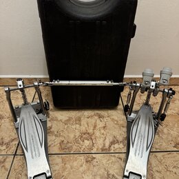Dvojpedál na bubny stříbrné barvy s černým kufrem v pozadí. Na obou pedálech je nápis speedcobras a na špičkách logo IZAMA. Na spojovací tyči je rovn…