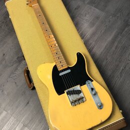 Žlutá elektrická kytara typu Telecaster položená na žlutém tvrdém kufru. Na hlavě hmatníku je viditelný nápis Fender. Kytara má černý pickguard, jede…