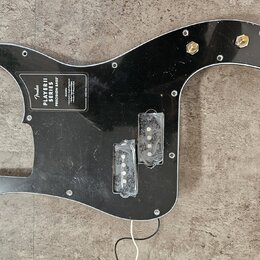 Černý plastový pickguard pro basovou kytaru s vyřezem pro snímače. Na povrchu je bílý nápis Fender PLAYER II SERIES PRECISION BASS s doplňujícími tex…