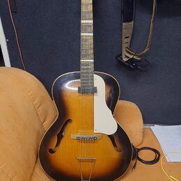 Polodupatá elektrická kytara s korpusem v přechodové barvě od žluté po černou. Nástroj má bílý plechový kryt (pickguard) a bílé ladičky na hlavě. Na…