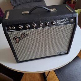 Černý kytarový kombozesilovač s šedou textilní maskou reproduktoru. Na horním ovládacím panelu jsou nápisy Princeton Reverb Amp, FENDER MUSICAL INSTR…
