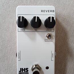 Bílý efekt pedál s nápisem REVERB v horní části. Obsahuje tři černé otočné ovladače s popisky VERB, EQ a DECAY, přepínač PRE-DELAY a v dolní části ná…
