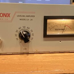 Šedý rackový procesor s nápisy TELETRONIX ENGINEERING CO, LEVELING AMPLIFIER MODEL LA-2A. Zařízení má v pravé části analogový VU metr s nápisem TELET…