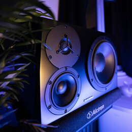 Černý studiový monitor s dvěma membránami a jedním výškem. Na spodní hraně je nápis DVR AUDIO, pod kterým se nachází zařízení s logem a nápisem Alctr…