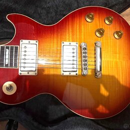 Elektrická kytara s tmelem v červeno-žlutém přechodu (sunburst) a Rounded body. Nástroj má dva snímače s bílými rámečky, čtyři zlaté ovládací knoflík…